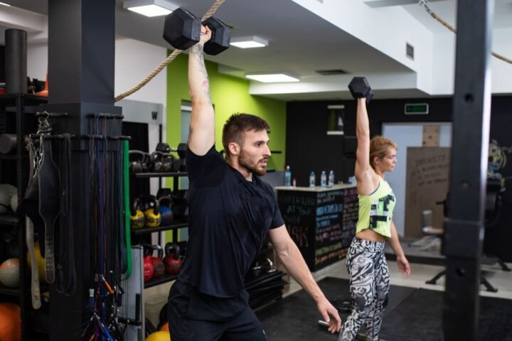 Man and woman perform dumbbell snatch in a gym