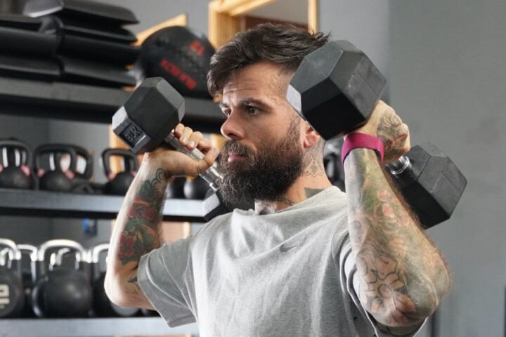 Scott Britton holding dumbbells by his shoulders wearing a pink Whoop tracker on his wrist