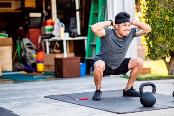 Man works out in front of his garage, performing unweighted squats.