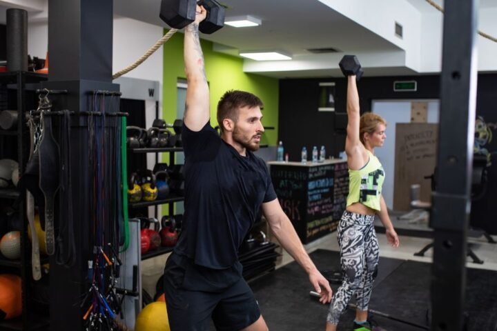 A man and woman performing a dumbbell snatch in a CrossFit box