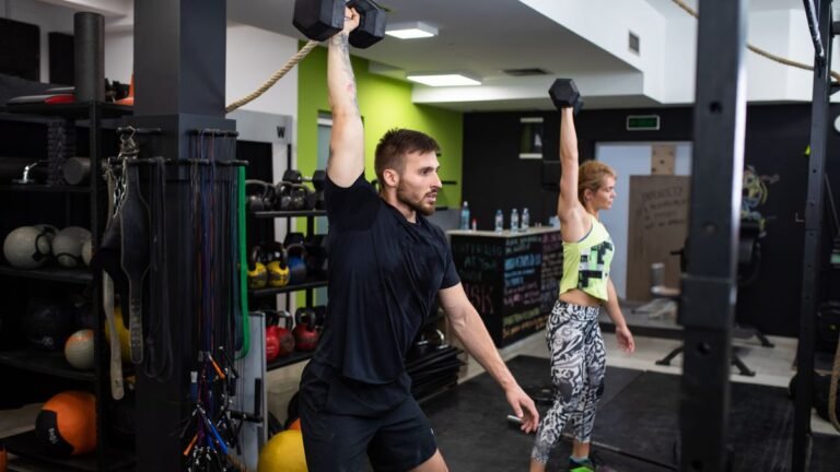 A man and woman performing a dumbbell snatch in a CrossFit box