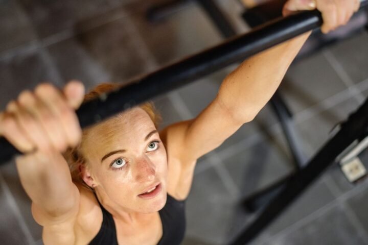 Woman gripping pull-up bar and looking up at it