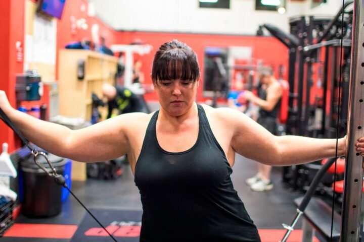 Woman using cable machine to perform lateral raise shoulder exercise