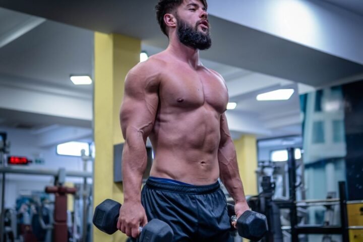 Shirtless bodybuilder in gym holding dumbbells