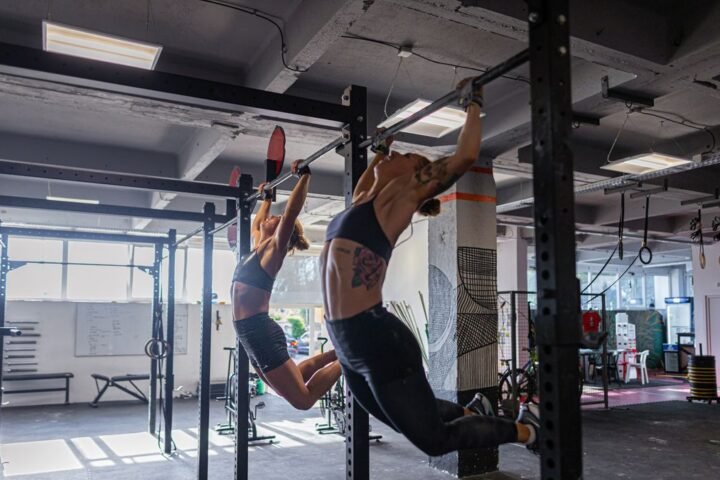 Two women performing kipping pull-ups in a gym